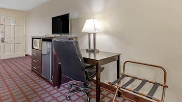 Ein Hotelzimmer mit Schreibtisch, Stuhl, Lampe, Fernseher und einer Minibar.