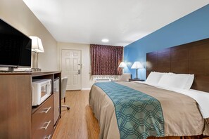 A hotel room with a bed, a desk with a microwave, a TV, and two lamps. - Econo Lodge Woodstock - Shenandoah Valley I-81 (Woodstock)