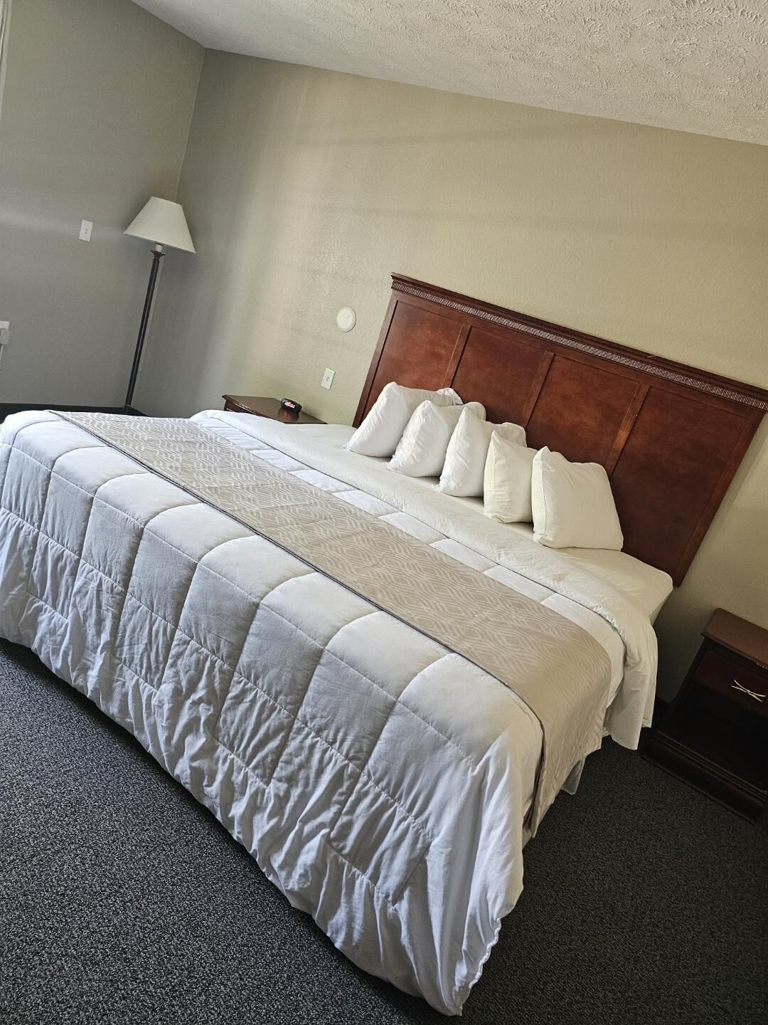 A hotel room with a large bed, a wooden headboard, a bedside table, and a lamp.