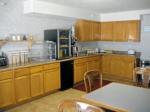 A compact kitchen with wooden cabinets, a refrigerator, and a dining table with chairs.