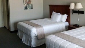 A hotel room with two beds, a painting on the wall, and a nightstand with two lamps.
