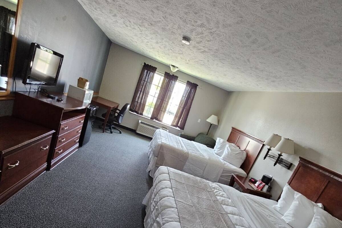 Quarto de hotel com duas camas, uma escrivaninha, uma cadeira, uma televisão e uma janela com cortinas.