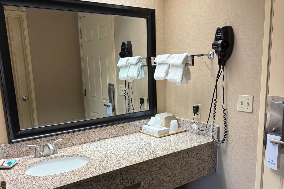 Un baño de hotel con lavamanos, espejo, toallero y secador de pelo.