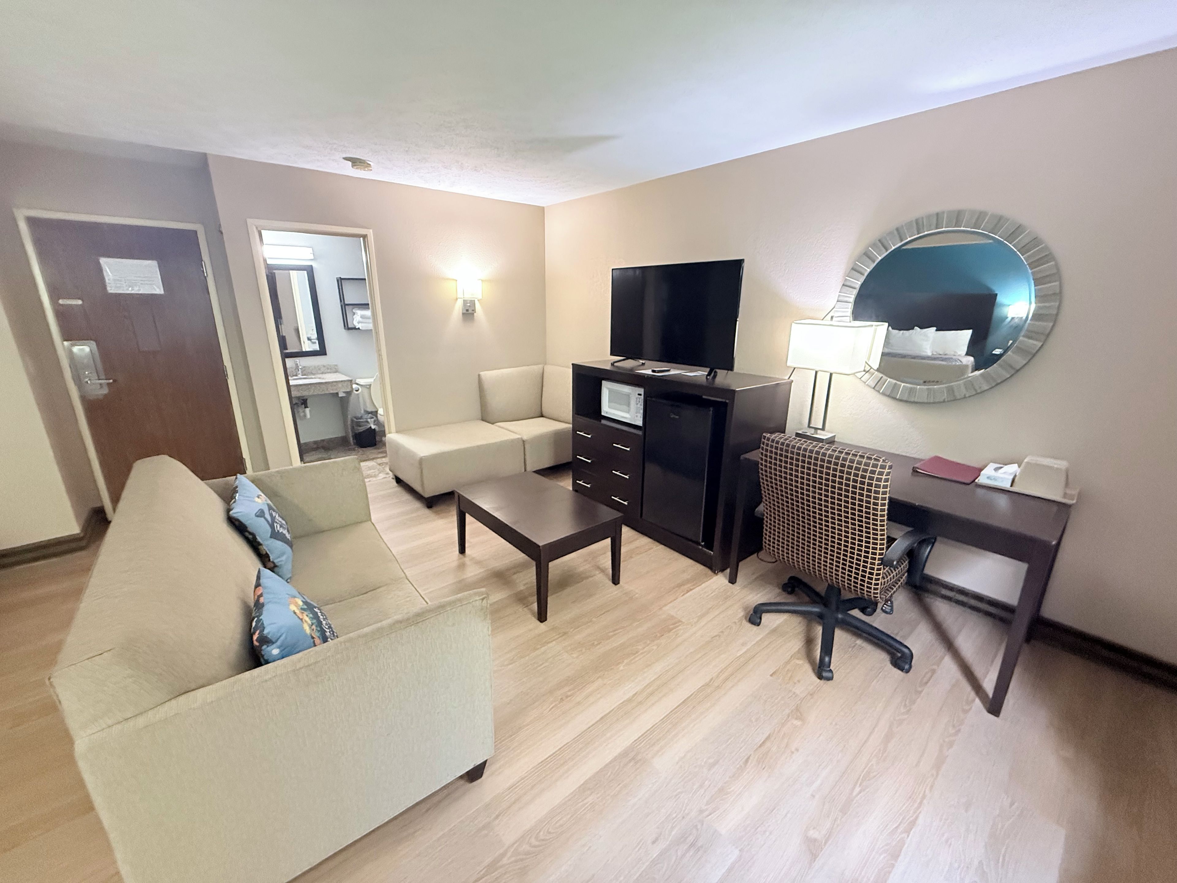 A hotel room with a sofa, a desk with a computer, a television, a microwave, and a small refrigerator.