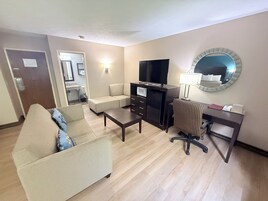 Habitación de hotel con sofá, escritorio con computadora, televisor, microondas y refrigerador pequeño.