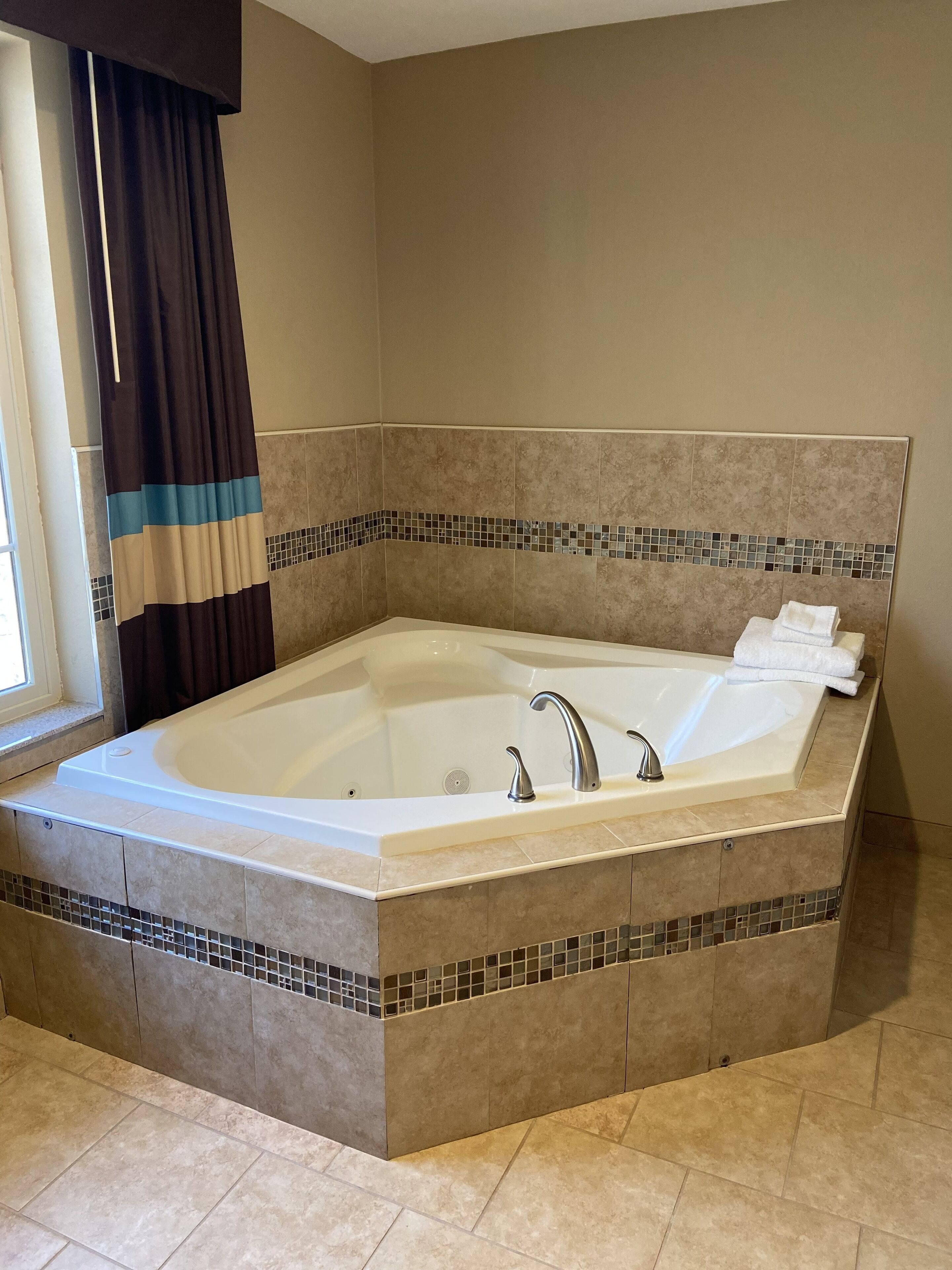 Una bañera grande y rectangular con un revestimiento de azulejos y una ventana pequeña con cortinas.