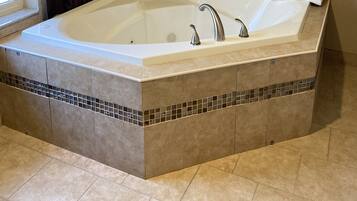 Una bañera grande y rectangular con un revestimiento de azulejos y una ventana pequeña con cortinas.