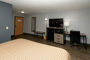 Quarto de hotel com cama, escrivaninha, computador, televisão e abajur.