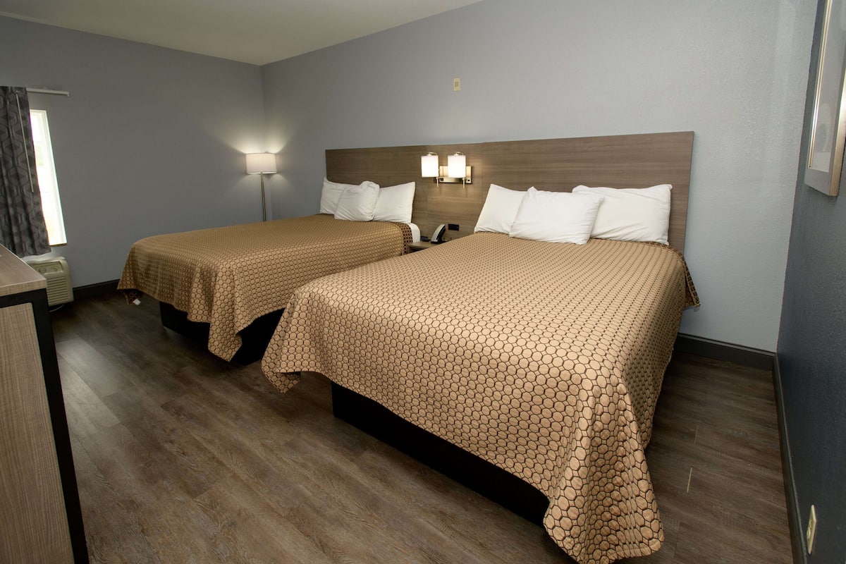 A hotel room with two beds, a nightstand, a lamp, and a window with curtains.