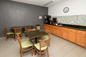 Una cocina pequeña y moderna con comedor. Incluye una mesa y sillas, una máquina de café y un reloj en la pared.