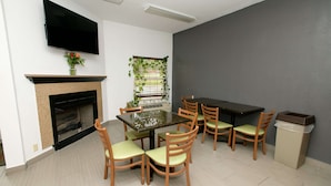 A dining area with a table and chairs, a fireplace, a TV mounted on the wall, and a window with plants. - Home Town Inn Ringgold (Ringgold)