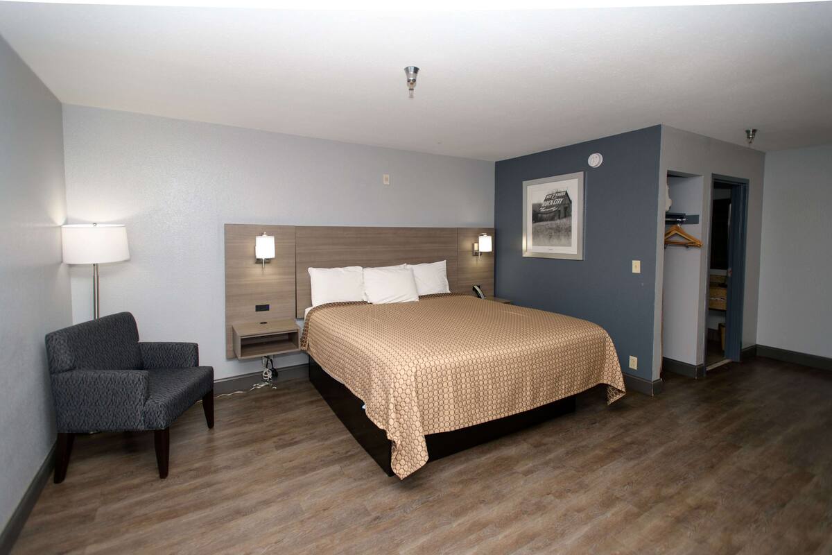 A hotel room with a bed, bedside tables, a chair, and a wardrobe.