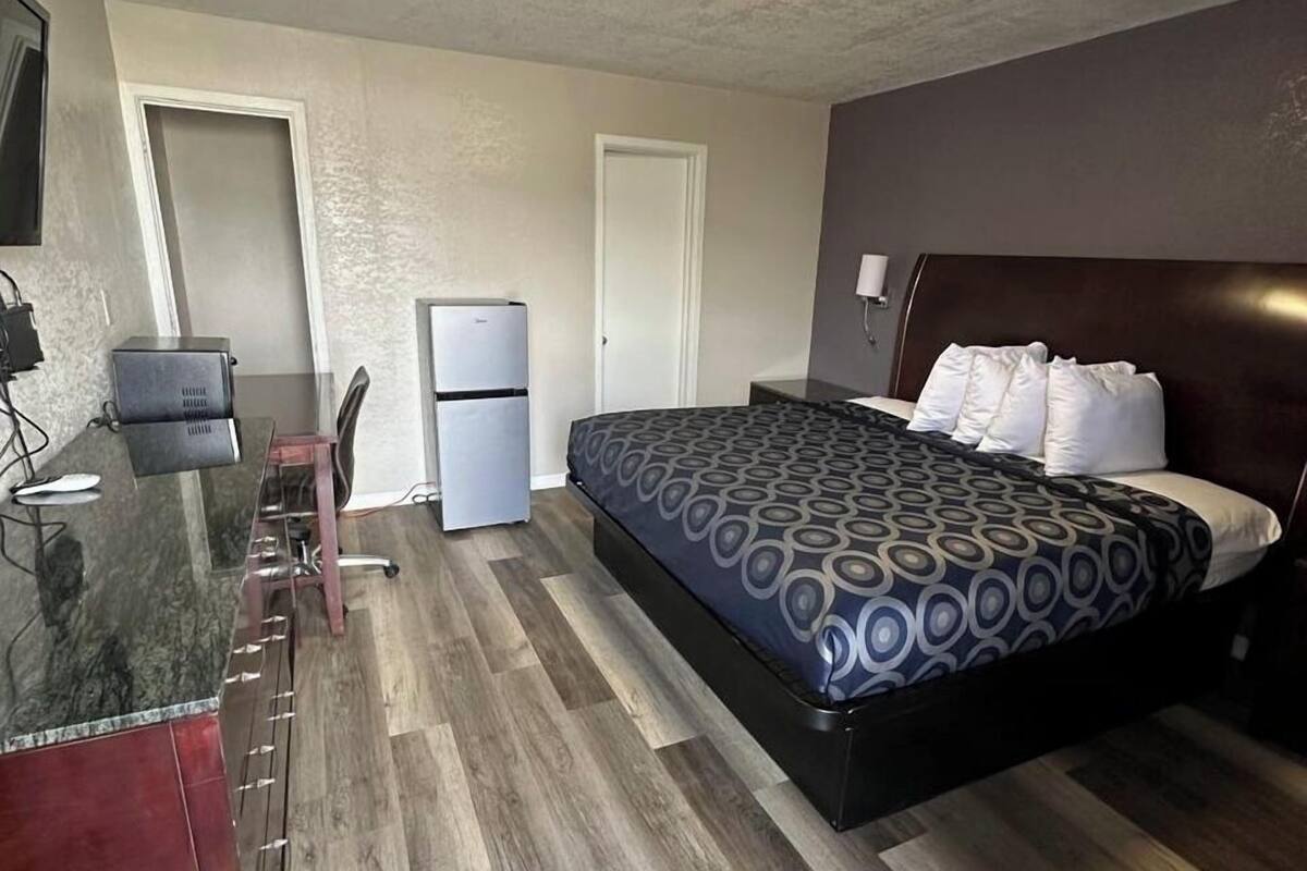 A hotel room with a bed, desk, refrigerator, and a television.