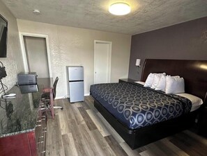 A hotel room with a bed, desk, refrigerator, and a television.
