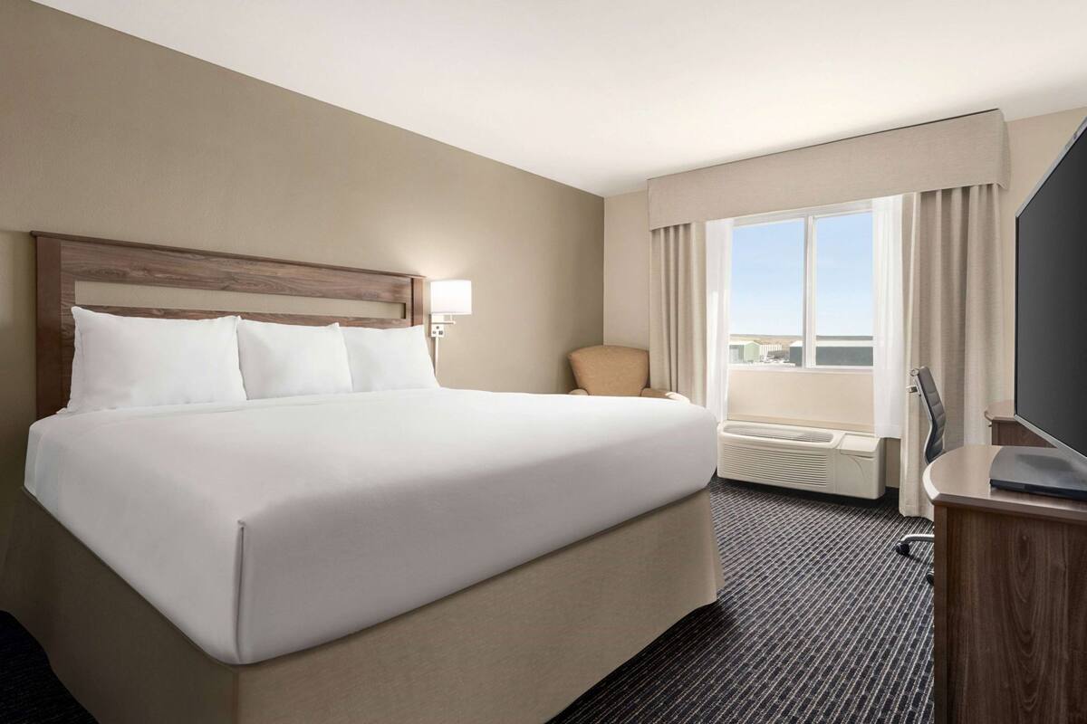 A hotel room with a large bed, a chair, a desk with a flat-screen TV, and a window with curtains.