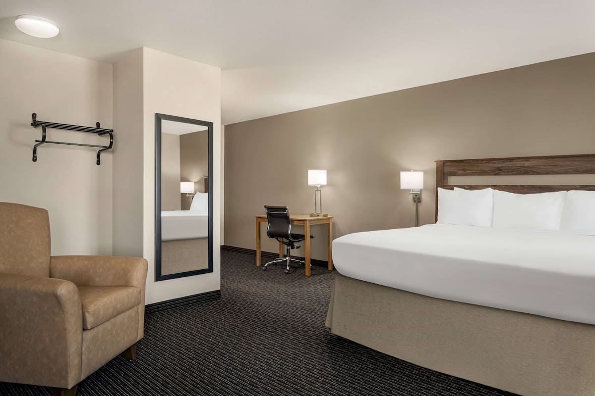 A hotel room with a bed, a chair, a desk, a lamp, and a mirror.