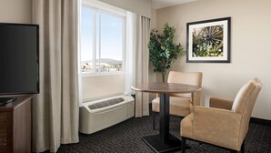 A hotel room with a large window, a flat-screen TV, a round table, two beige armchairs, a potted plant, and a framed picture on the wall. - Baymont by Wyndham Rawlins (Rawlins)