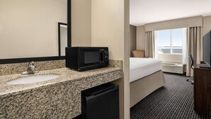 A hotel room with a granite countertop sink, a black microwave, a small black refrigerator, a bed with beige bedding, a TV, and a window with curtains. - Baymont by Wyndham Rawlins (Rawlins)