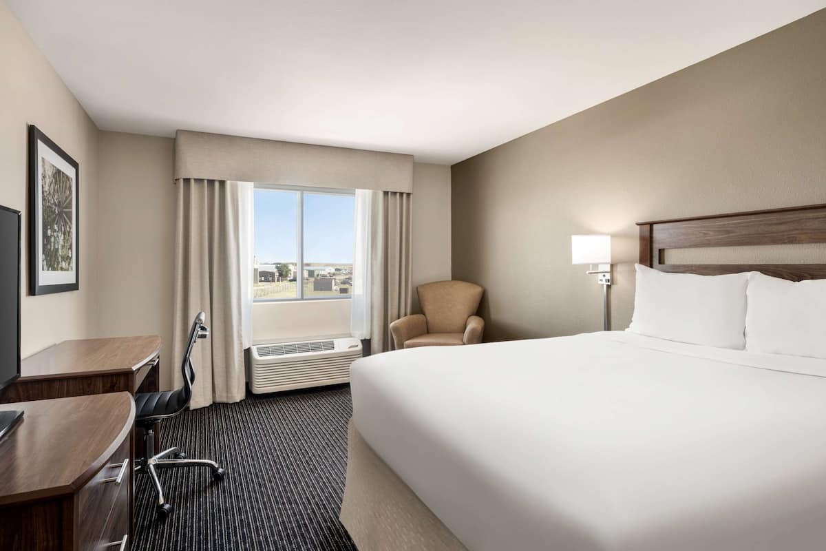 A hotel room with a large bed, a desk, a chair, a window with curtains, and a view of the city.