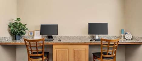 A workspace with two chairs, a desk, two monitors, a plant, and a clock.