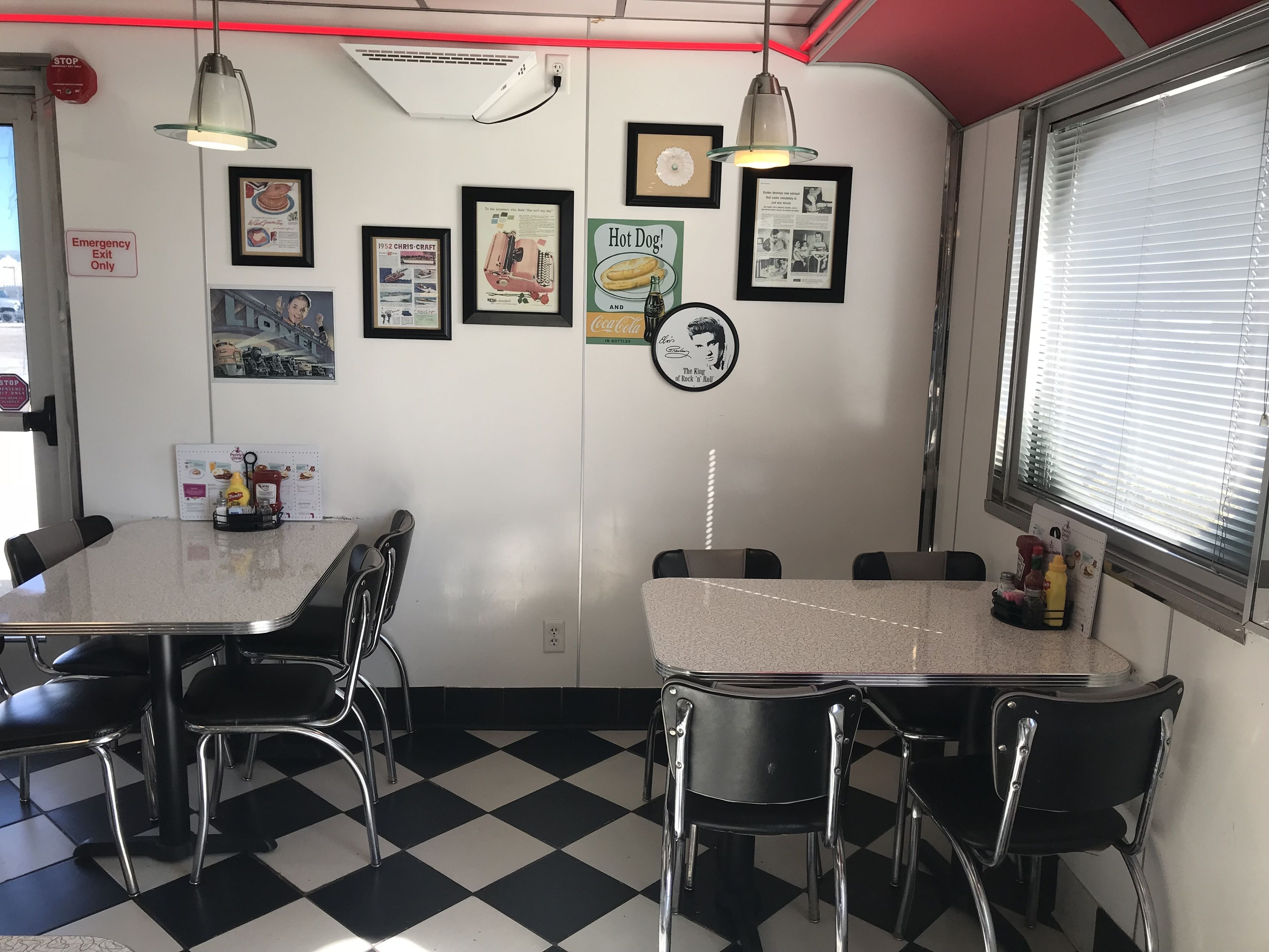Een eetcafé met geruit vloer, metalen stoelen en een toonbank met een menu.