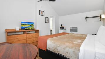 Quarto com cama, cômoda de madeira, ventilador de teto, TV fixada na parede e janela.