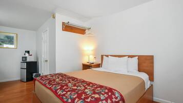 A hotel room with a bed, a nightstand with a lamp, a coat rack, a microwave, and a refrigerator.