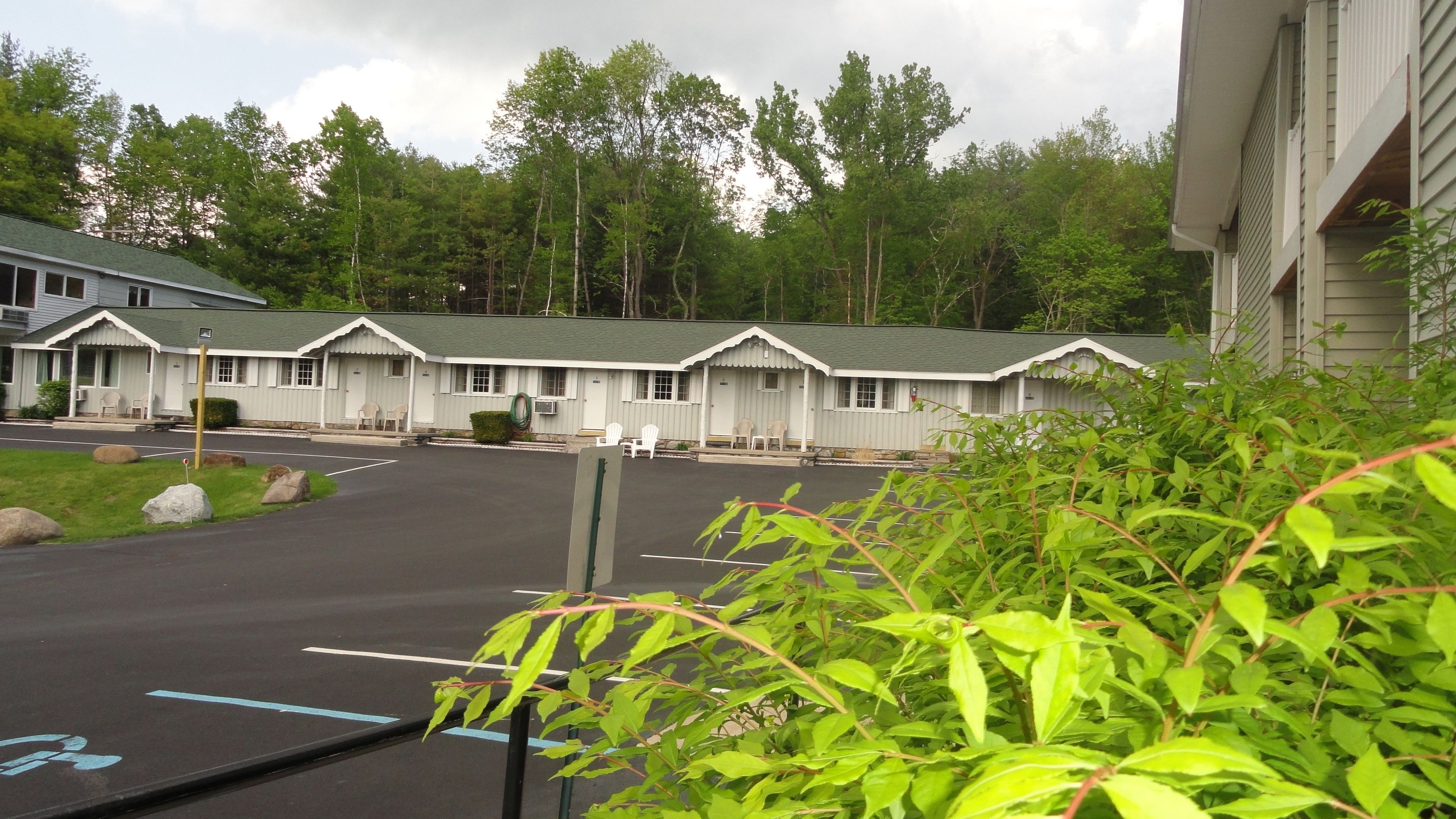 A row of motel-style buildings with attached parking spaces, surrounded by greenery.