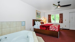 Una habitación de hotel con una cama grande, un ventilador de techo, una ventana con cortinas, una puerta y una bañera.