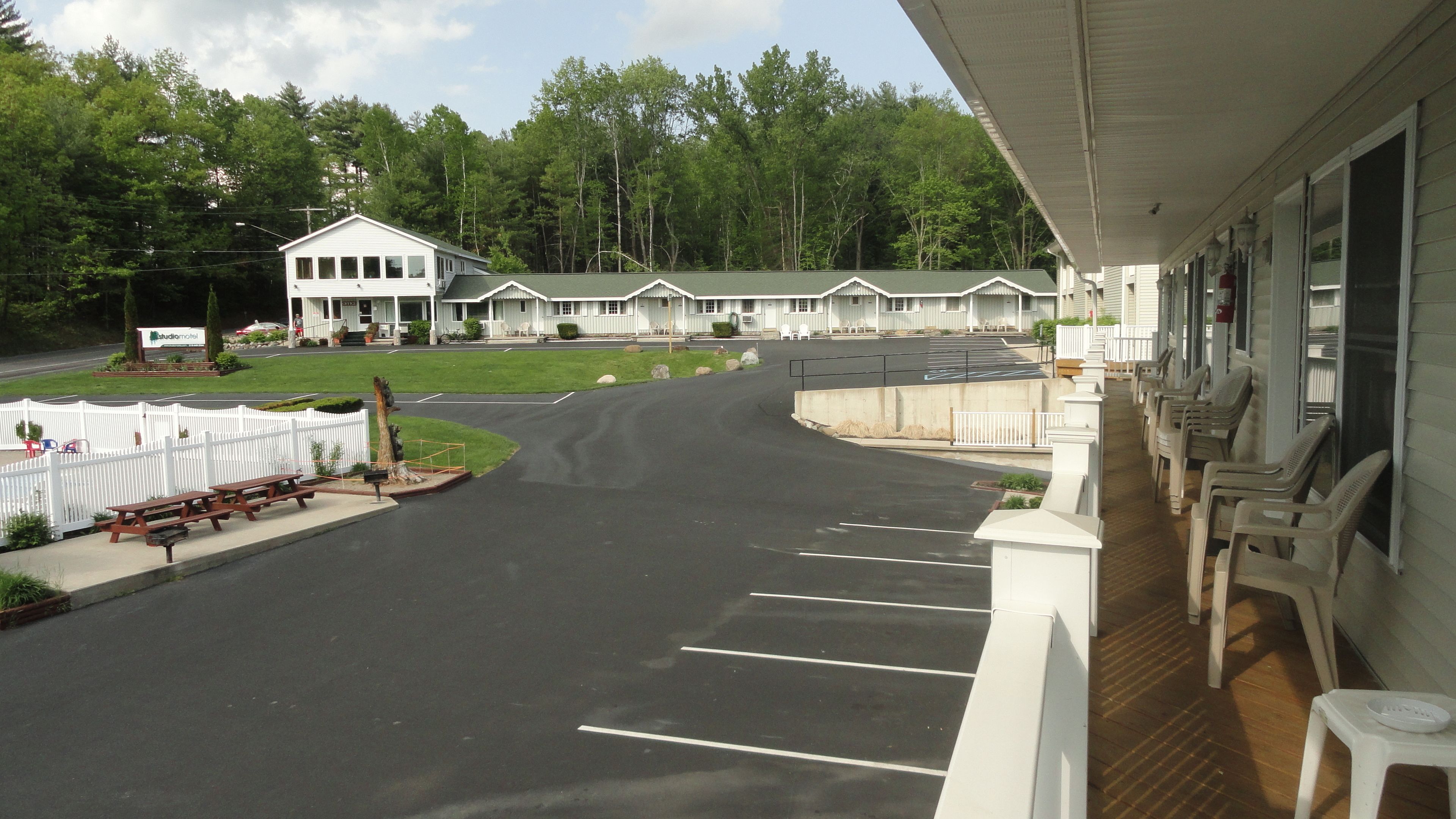 A motel with a parking lot, a covered porch with chairs, and a lawn area.