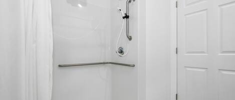 A white shower enclosure with a grab bar, a door, and a marble-tiled floor.