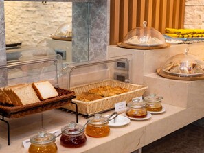 Un buffet proposant du pain, des viennoiseries et diverses confitures.
