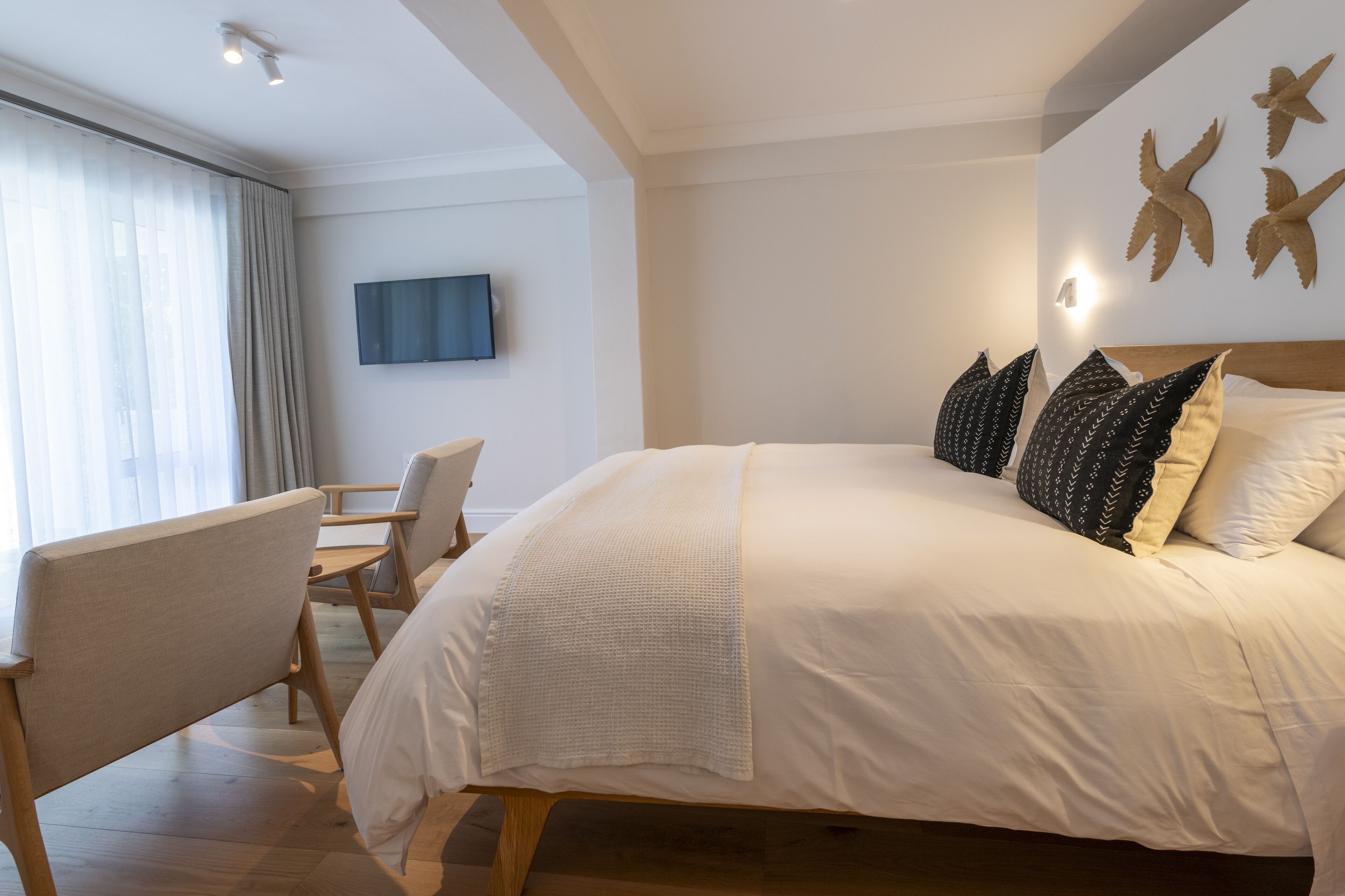 A modern hotel room with a large bed, a flat-screen TV mounted on the wall, and a seating area with chairs.