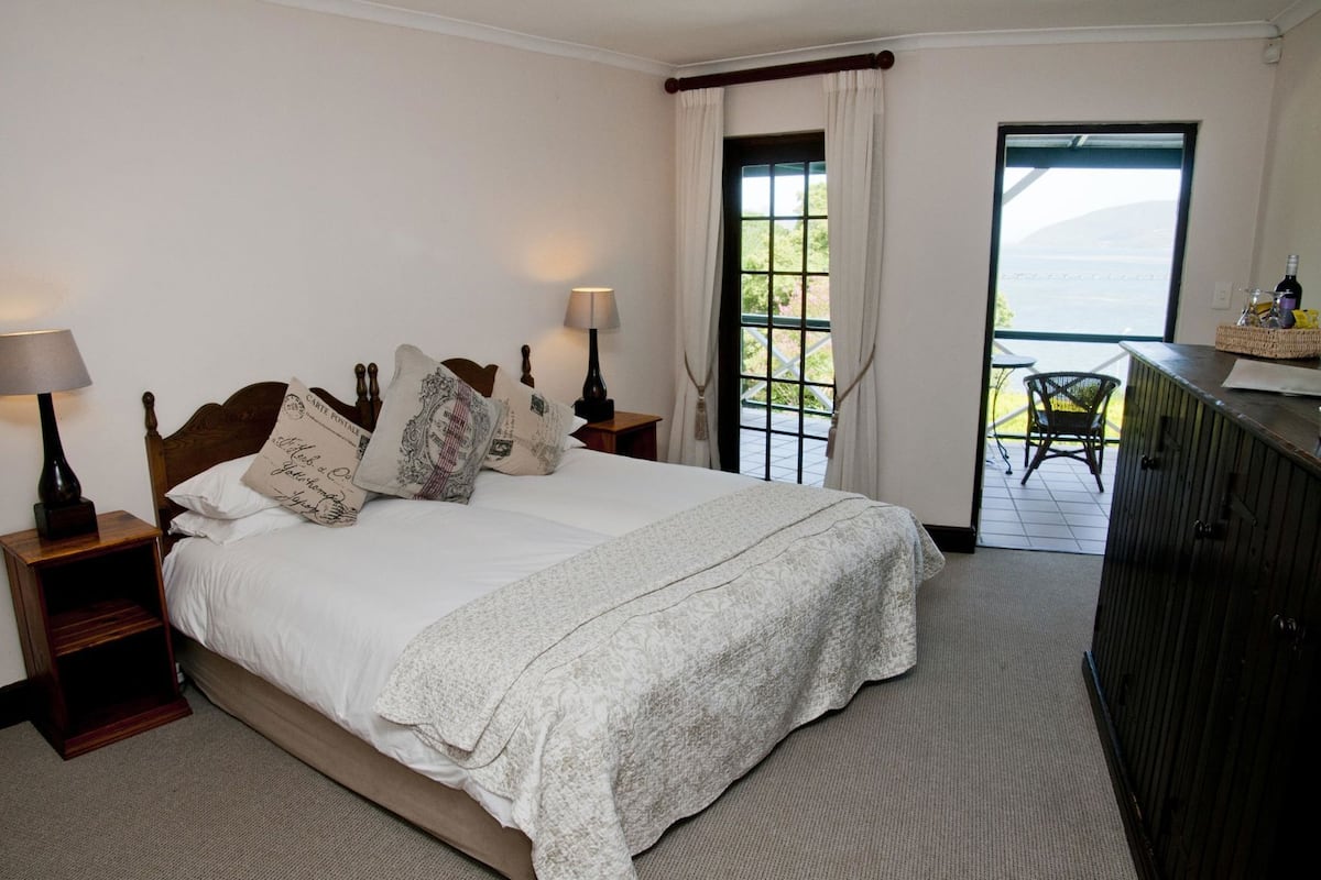 A bedroom with a bed, two bedside tables with lamps, a window with curtains, and a view of the outdoors.