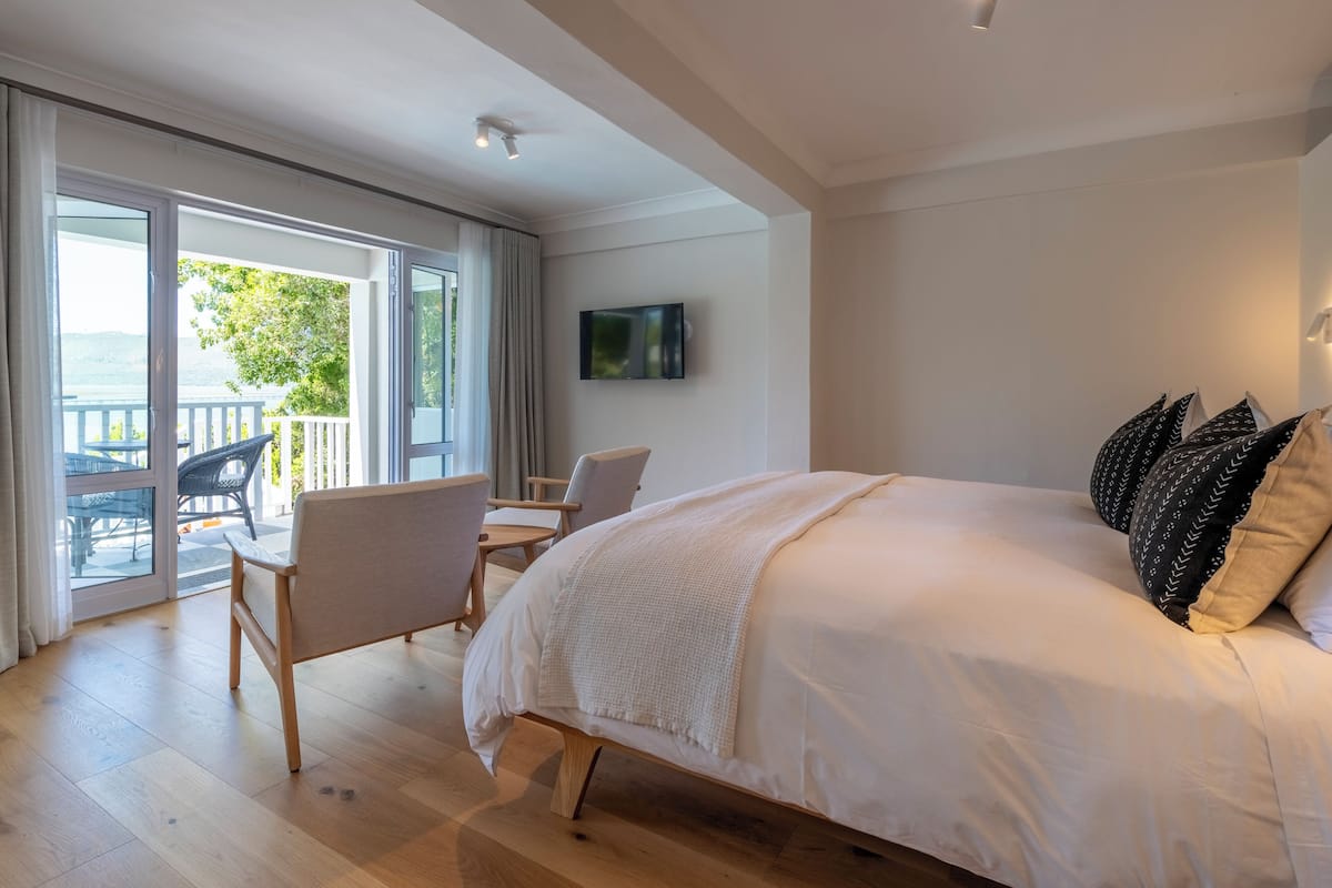 A bedroom with a large bed, a TV on the wall, and a balcony with outdoor furniture.