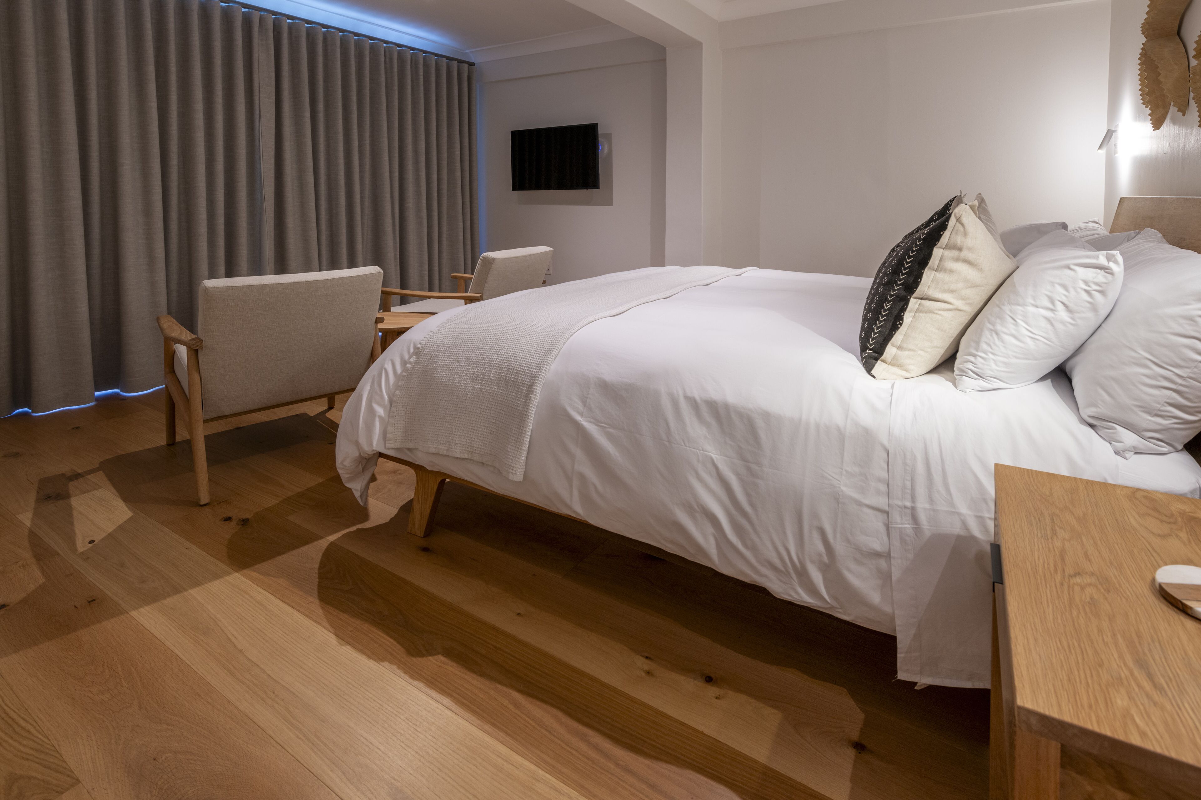 A modern bedroom with a large bed, a wooden desk, a chair, and a TV mounted on the wall.