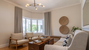 A modern living room with a wooden coffee table, two armchairs, a sofa, and a large window with curtains. - Hide Away Guest House (Knysna)