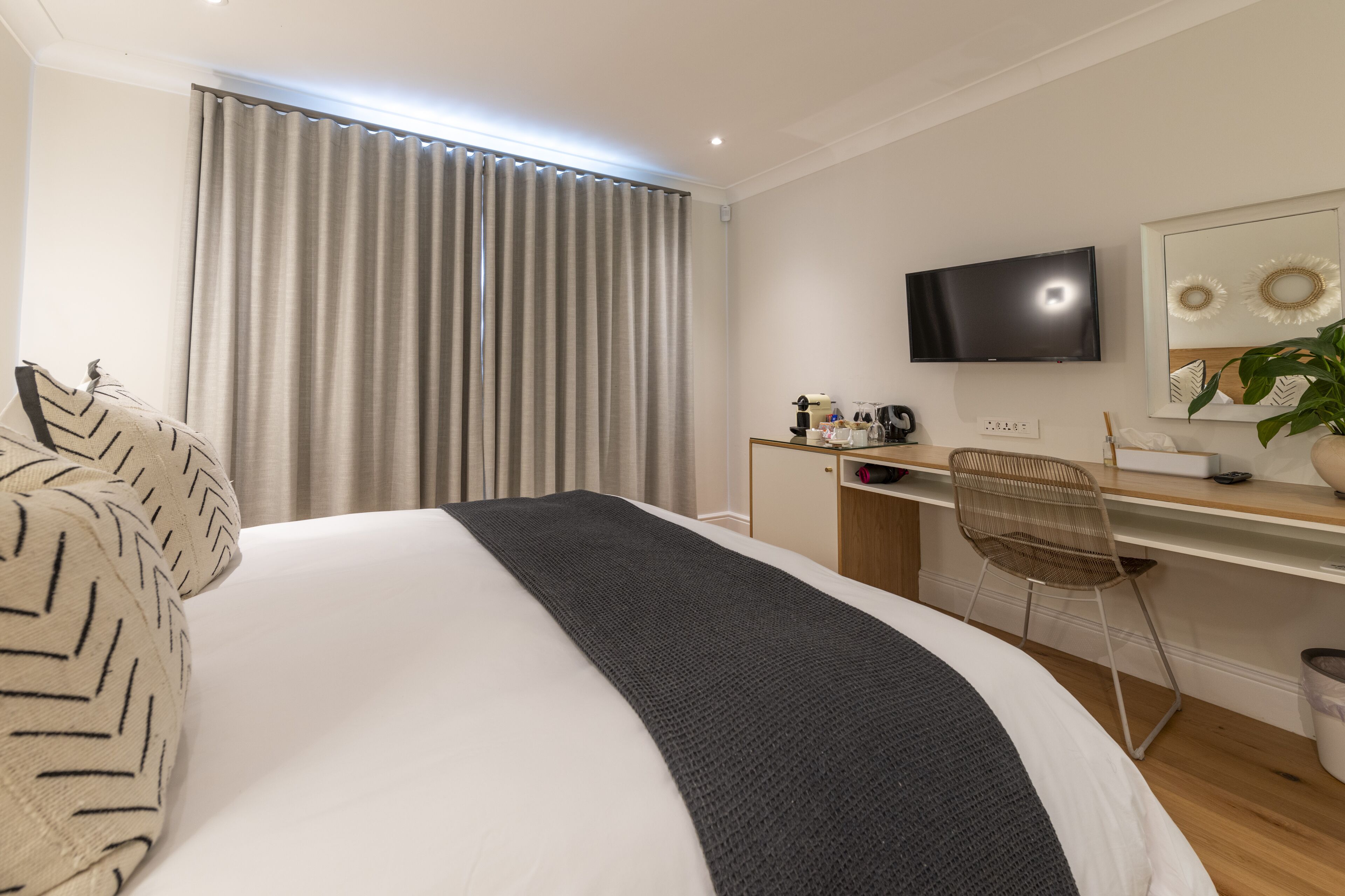 Een hotelkamer met een groot bed, een bureau met stoel, een televisie en een raam met gordijnen.