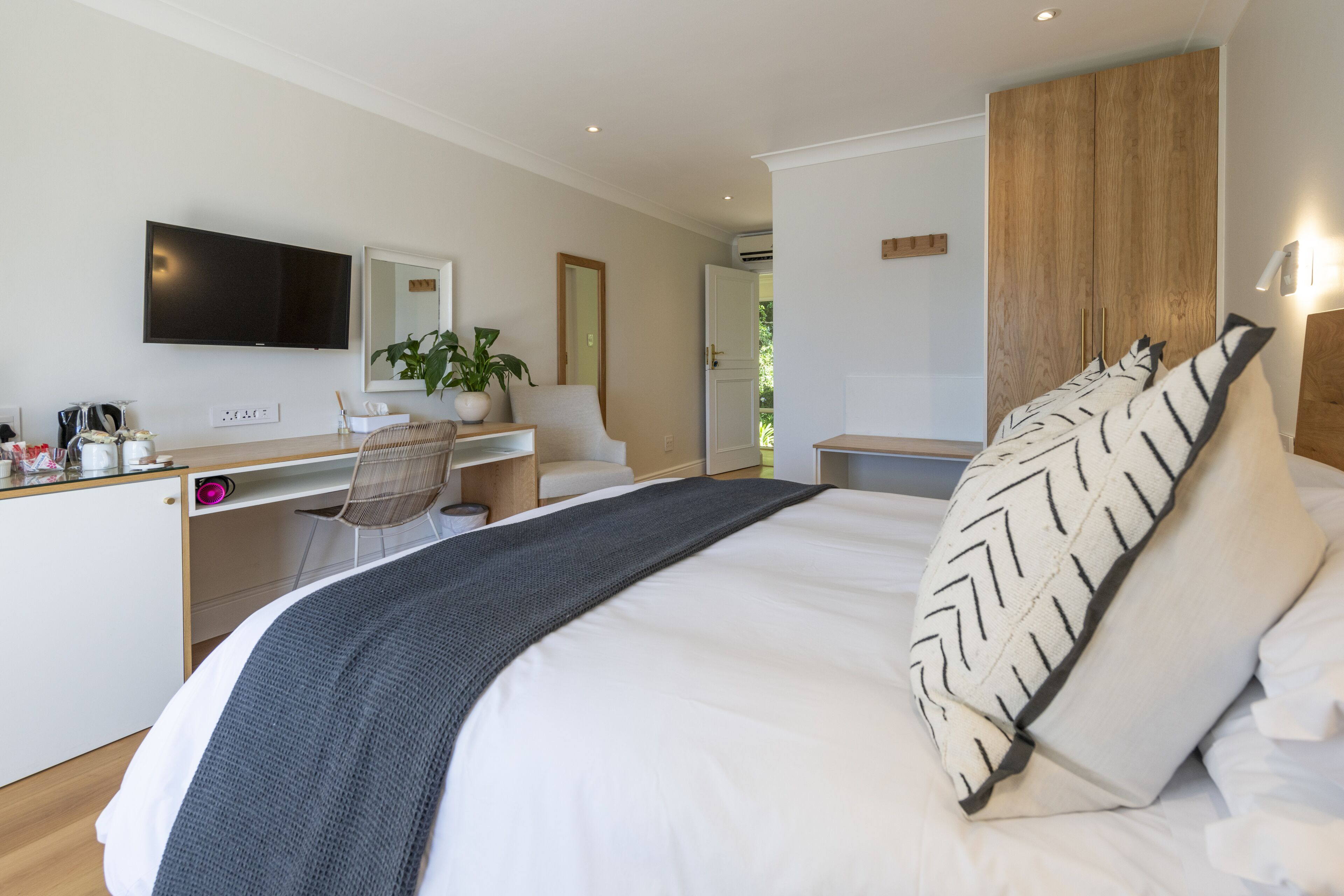 Una habitación de hotel moderna con una cama grande, un escritorio con una computadora, una silla, un televisor y un armario.