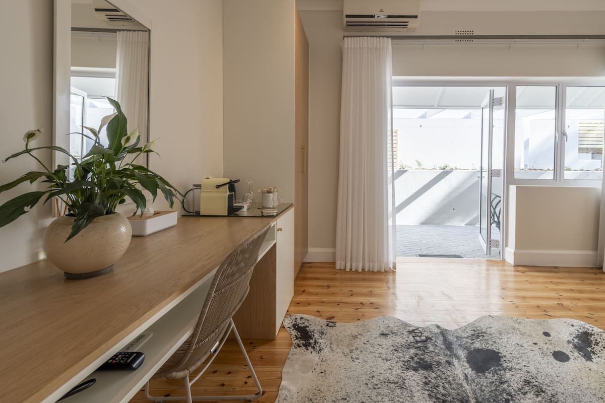 A modern room with a wooden desk, a large mirror, a potted plant, and a view of the outdoors through a sliding glass door.
