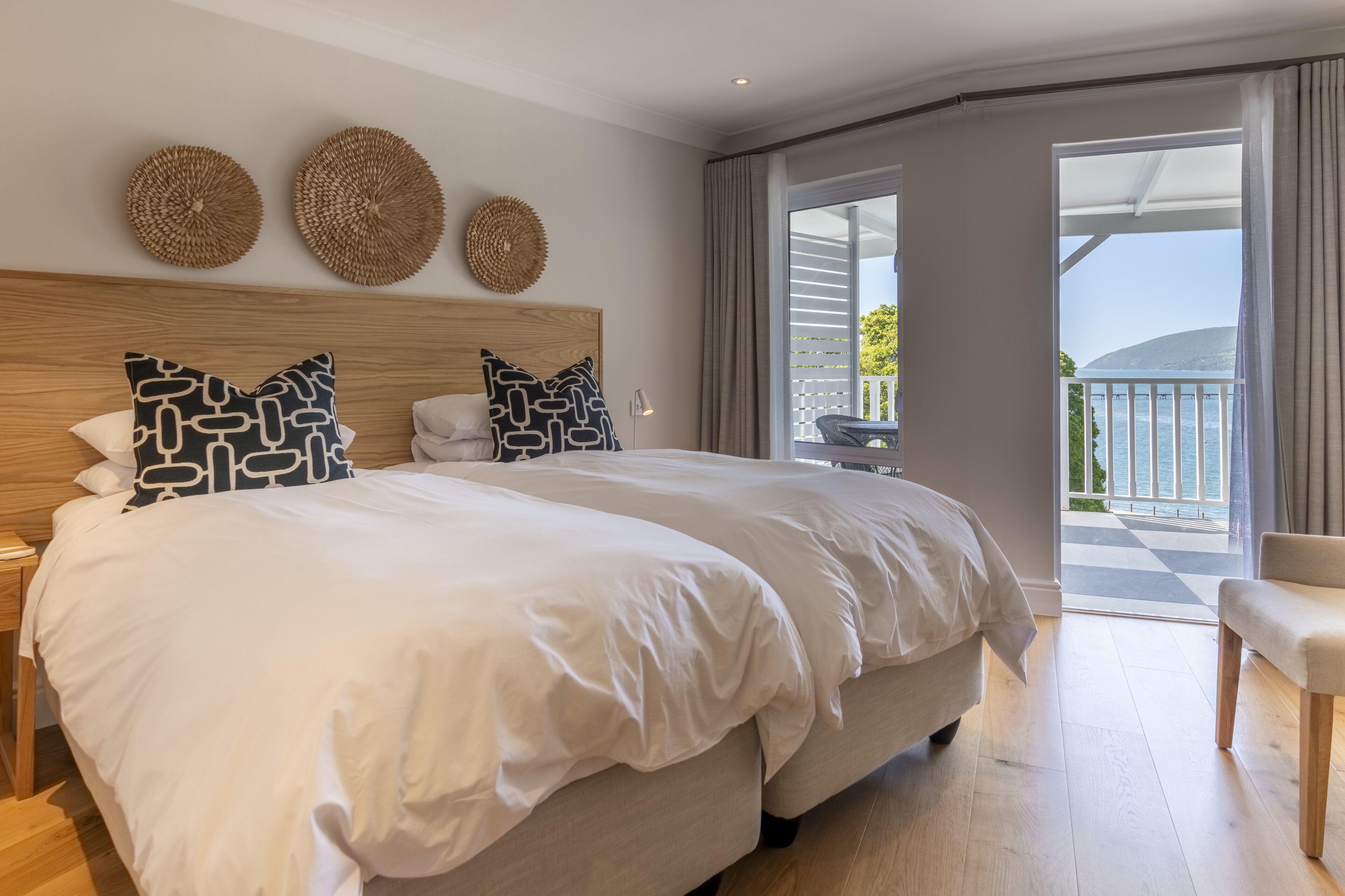 A spacious bedroom with a large bed, a wooden headboard, and a balcony with a view of the sea.