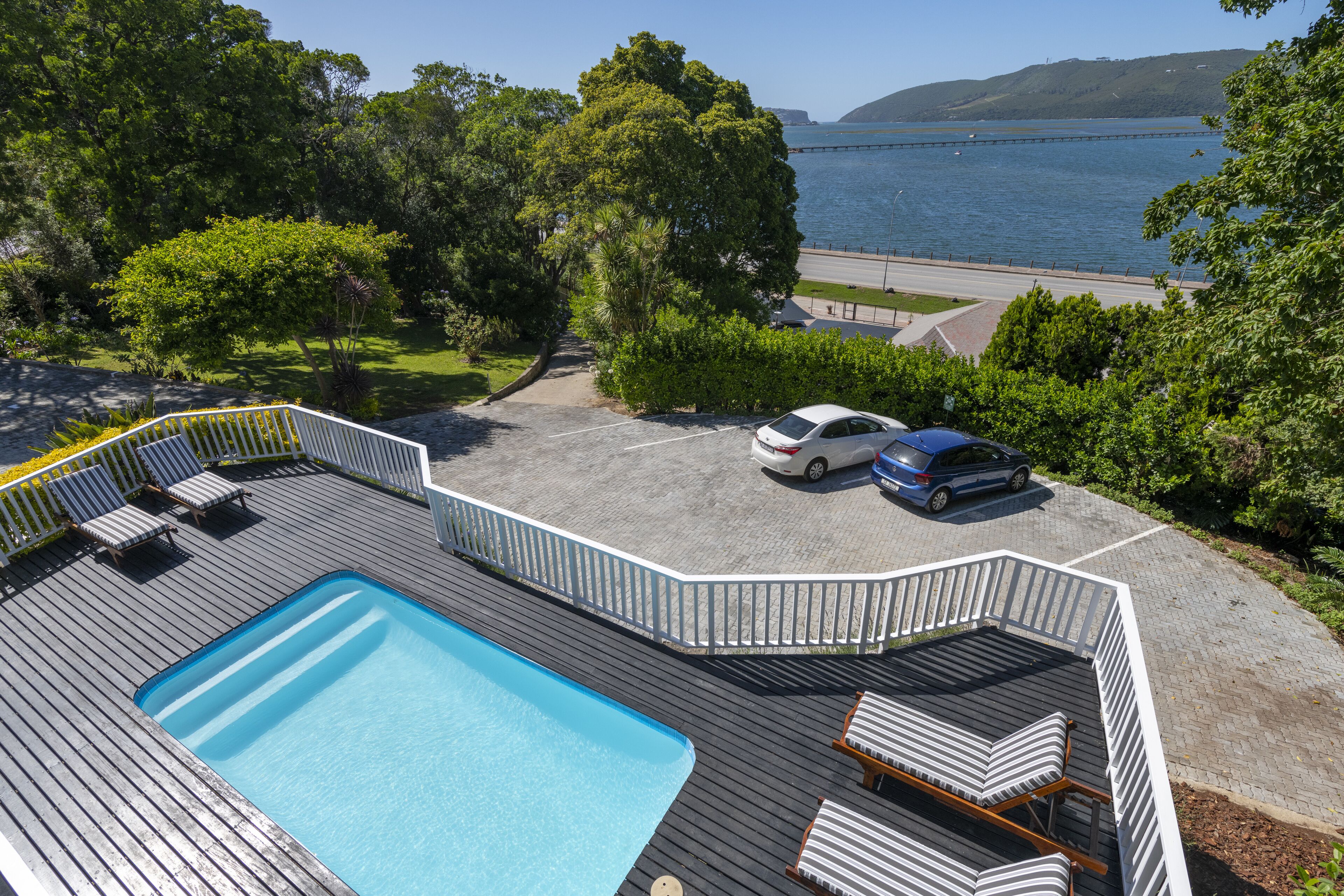 A wooden deck with a swimming pool, lounge chairs, and a view of the sea.