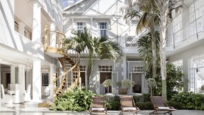 A spacious indoor pool area with a wooden spiral staircase, lounge chairs, and lush greenery.