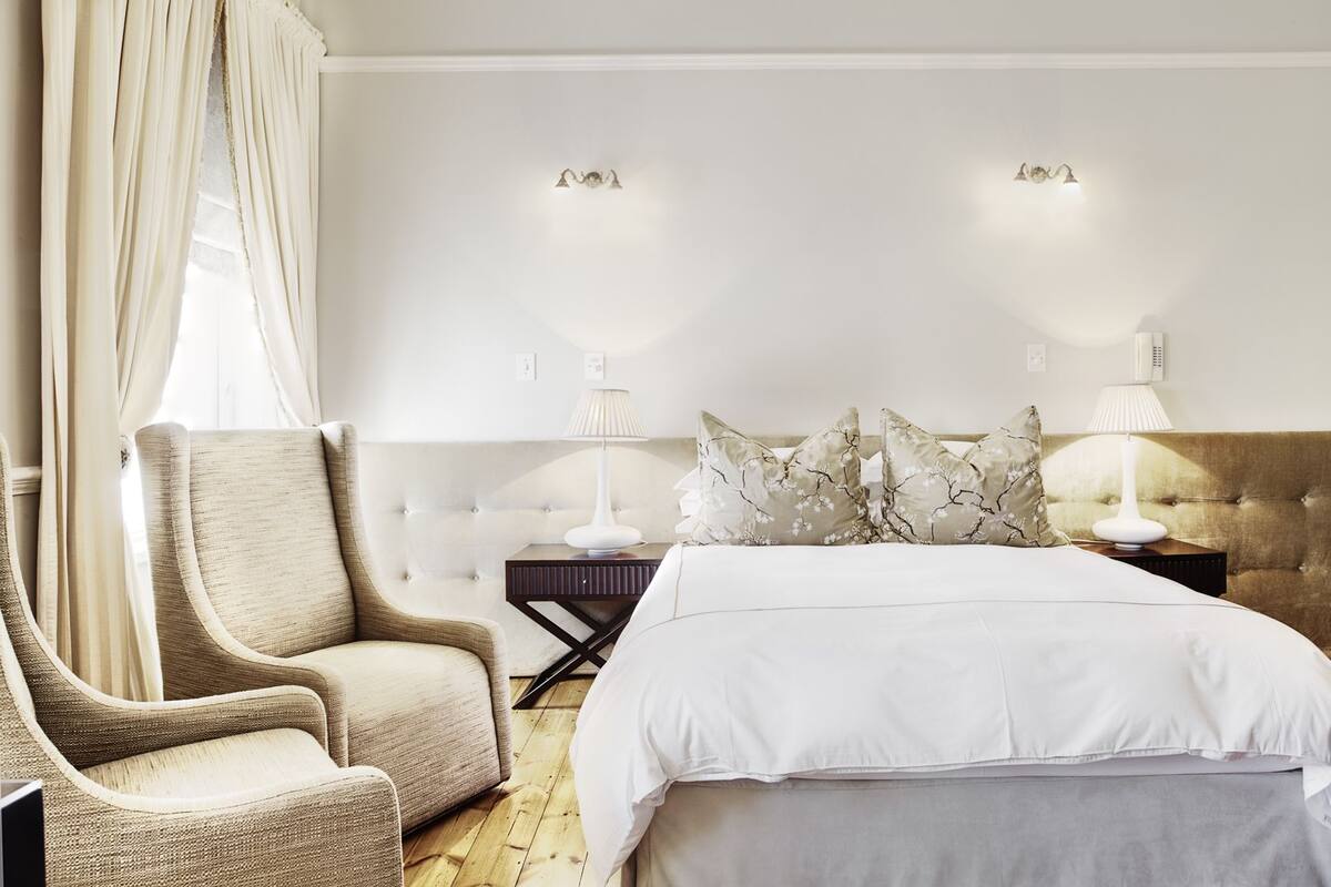 A bedroom with a bed, a chair, two bedside tables with lamps, and a window with curtains.