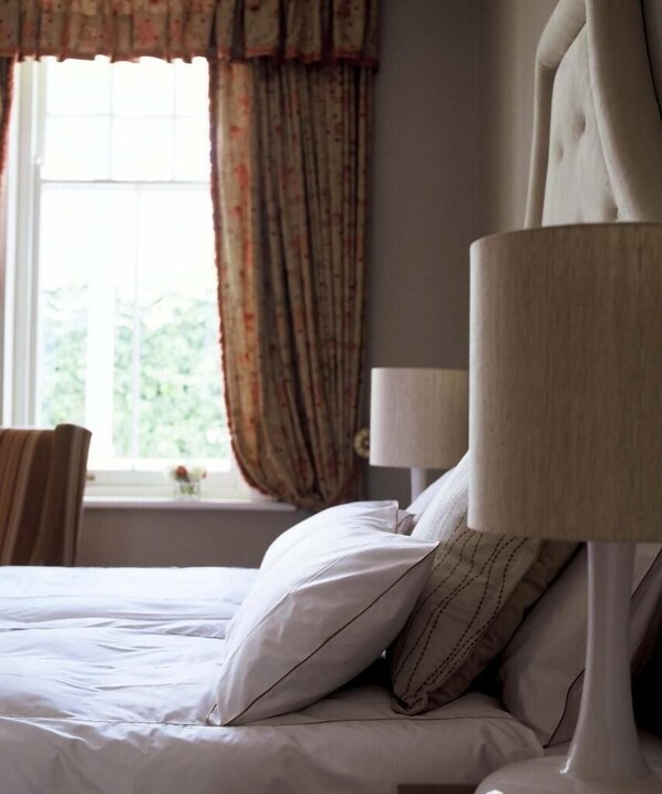 A neatly made bed with a headboard, a bedside lamp, and a window with curtains. - Banksia Boutique (Cape Town)