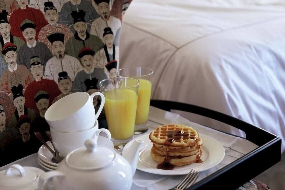 A hotel room with a neatly made breakfast tray including waffles, juice, and tea set.