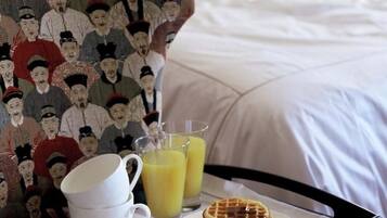 Bandeja de desayuno con waffles, jugo y té sobre una cama con ropa blanca.