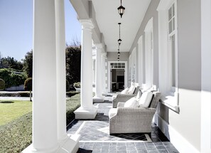 A covered porch with two wicker chairs, white columns, and a tiled floor. - Banksia Boutique (Cape Town)