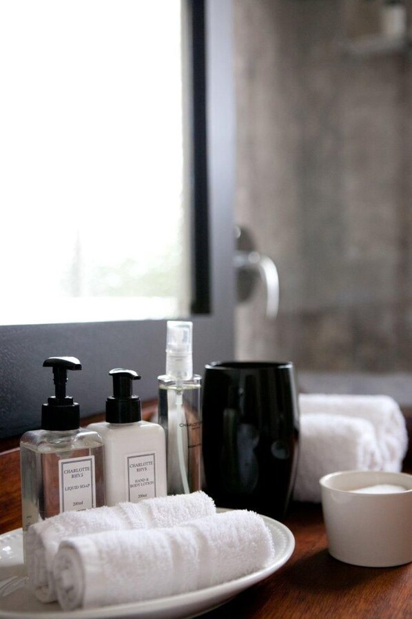 Une salle de bain avec des articles de toilette disposés sur un plateau, notamment des flacons de savon et de lotion, une tasse et des serviettes.