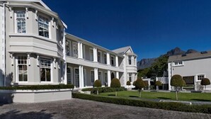 A large, white, multi-story building with a symmetrical facade, multiple windows, and a well-maintained lawn with trimmed bushes.